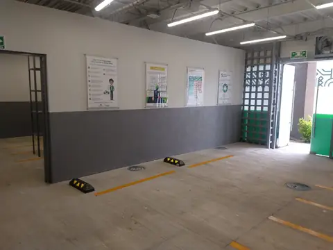 Área interior con muro gris, avisos de seguridad y topes de estacionamiento amarillos