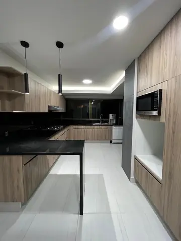 Cocina terminada: barra negra, luminarias colgantes y torre de microondas empotrado