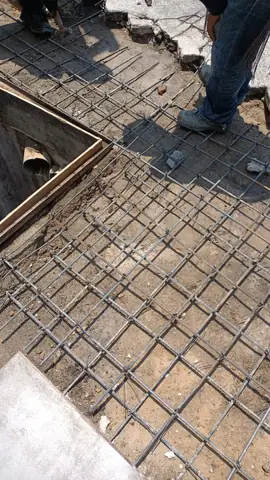 Malla de acero de refuerzo armada en un registro, junto al piso de adoquín